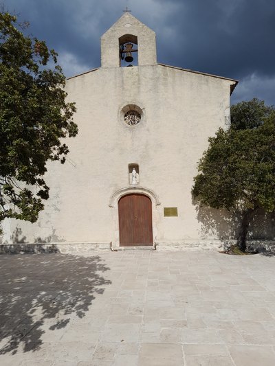 Façade principale de la chapelle composée d'une cloche au sommet, un œil de bœuf, une statue de la Vierge Marie et une porte