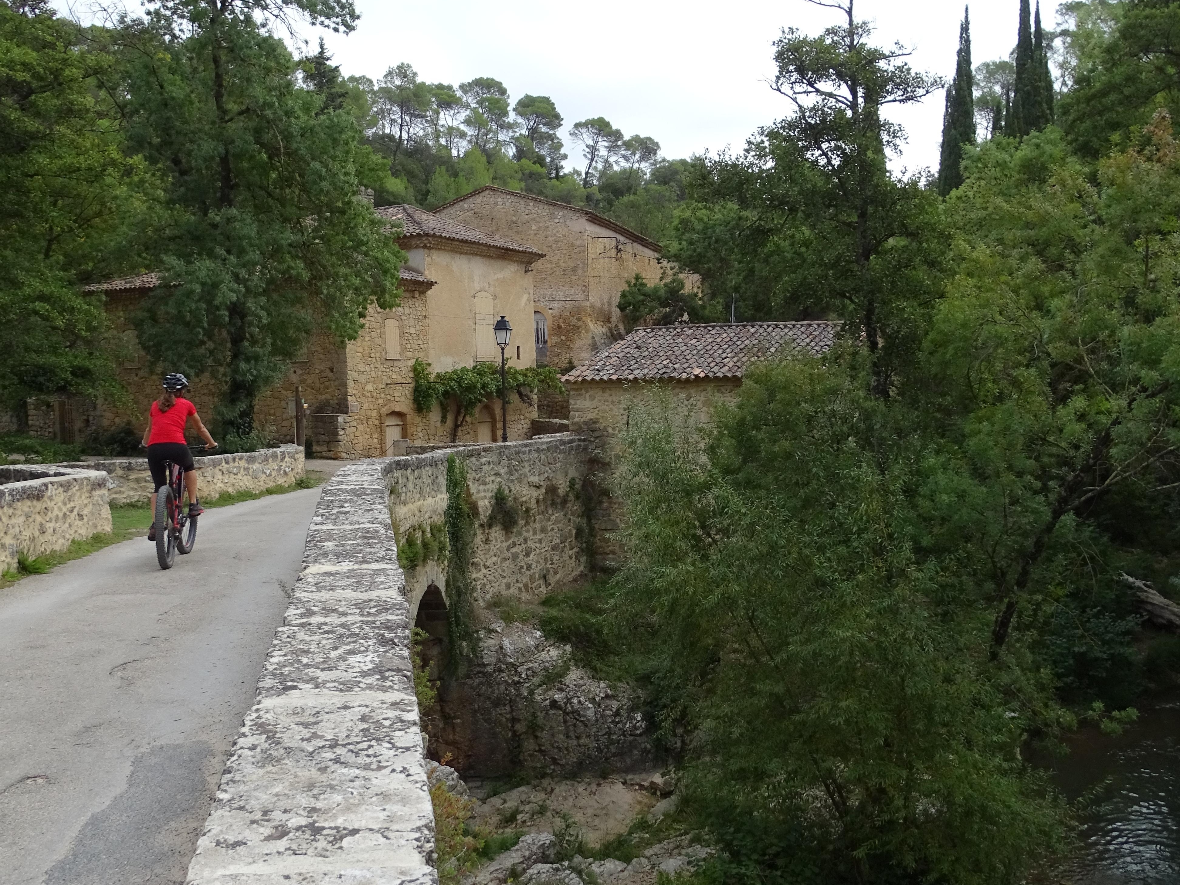 VTTiste roulant sur une route bordée par des murets en pierre, avec une vue sur la rivière en contrebas
