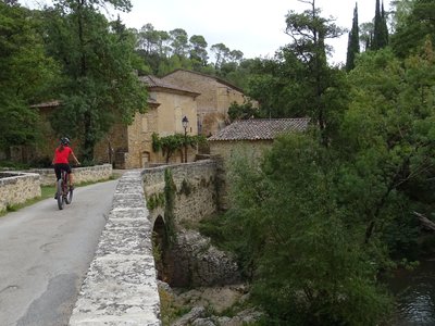 VTTiste roulant sur une route bordée par des murets en pierre, avec une vue sur la rivière en contrebas