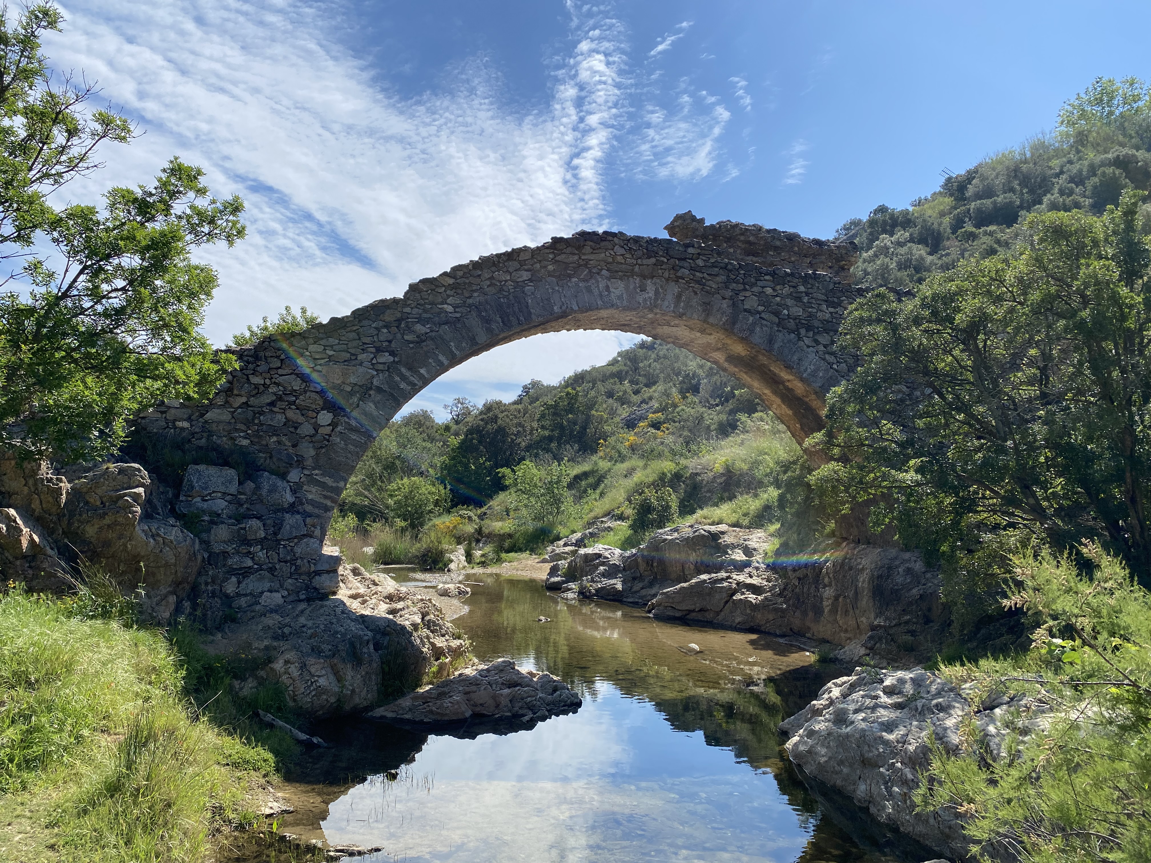 Pont en pierres apparentes enjambant une petite rivière entouré de végétation méditerranéenne