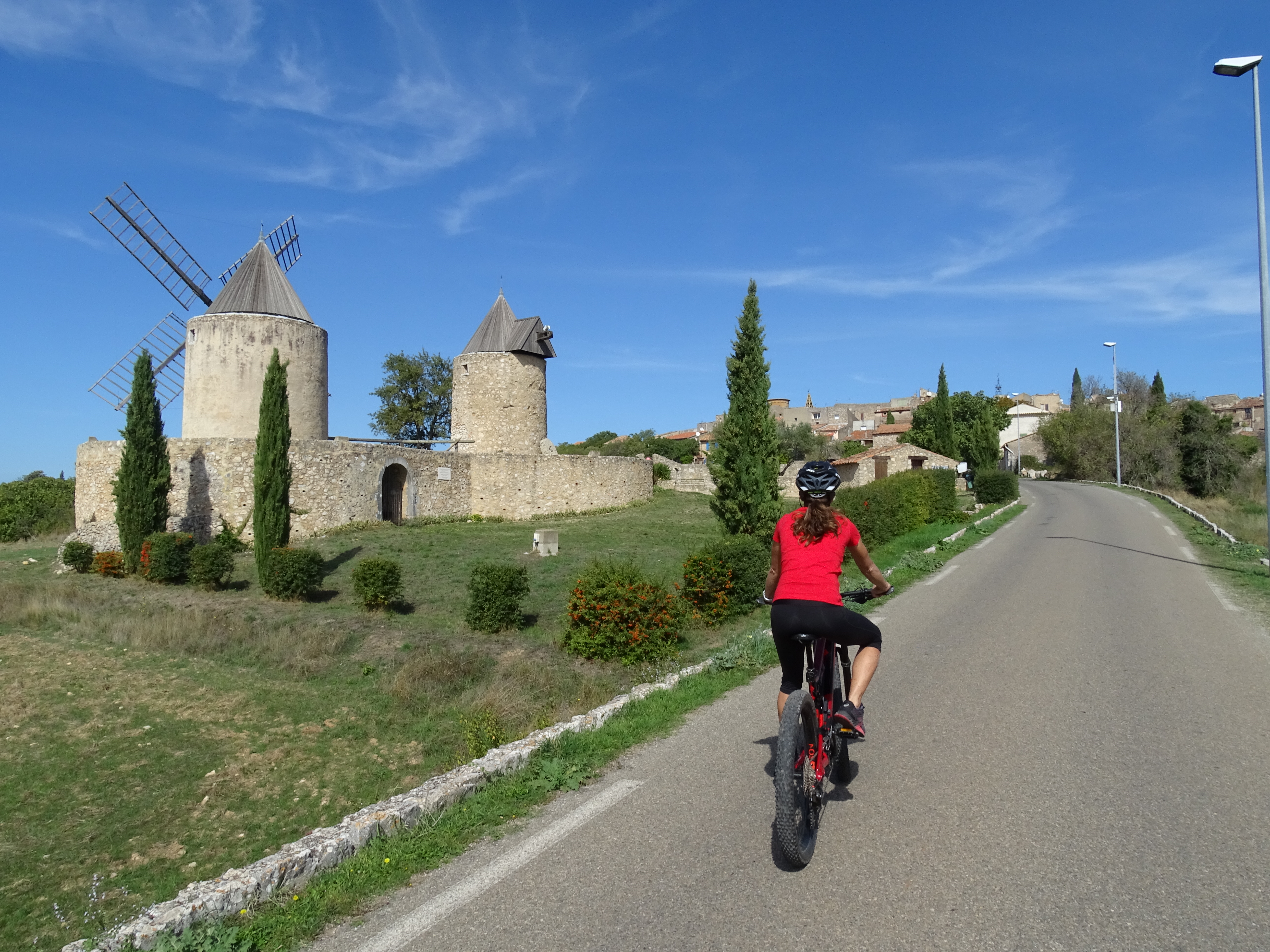 Cycliste sur route goudronnée avec en deuxième plan les 2 moulins en pierres à l'entrée d'un pré