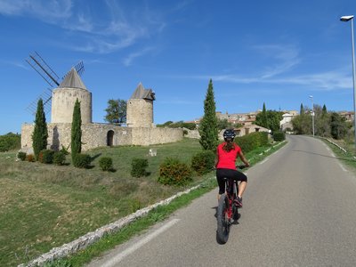 Cycliste sur route goudronnée avec en deuxième plan les 2 moulins en pierres à l'entrée d'un pré